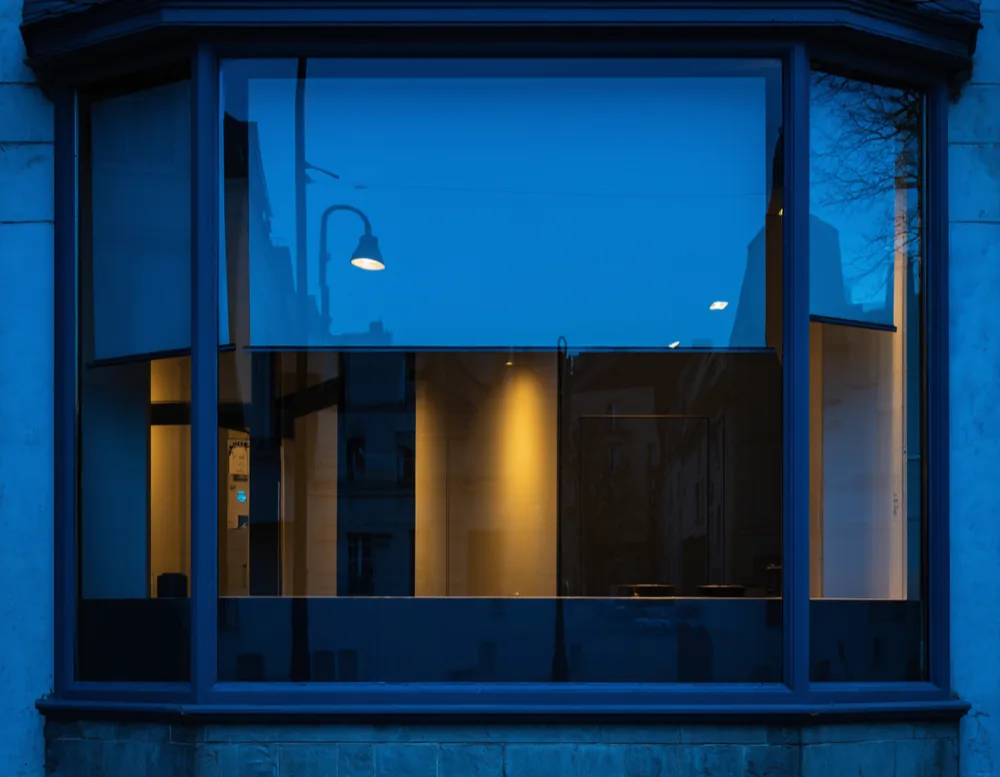 A large shopfront window at dusk with warm light inside and clean glass