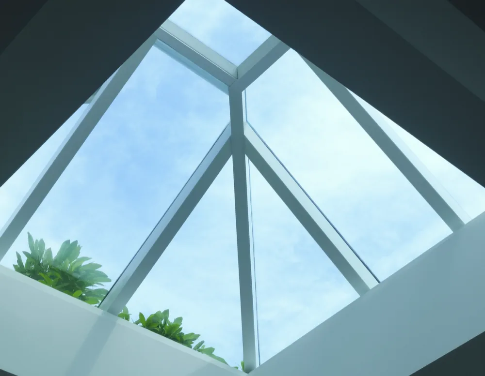 The glass roof of a conservatory seen from inside with rafters and pale blue sky above